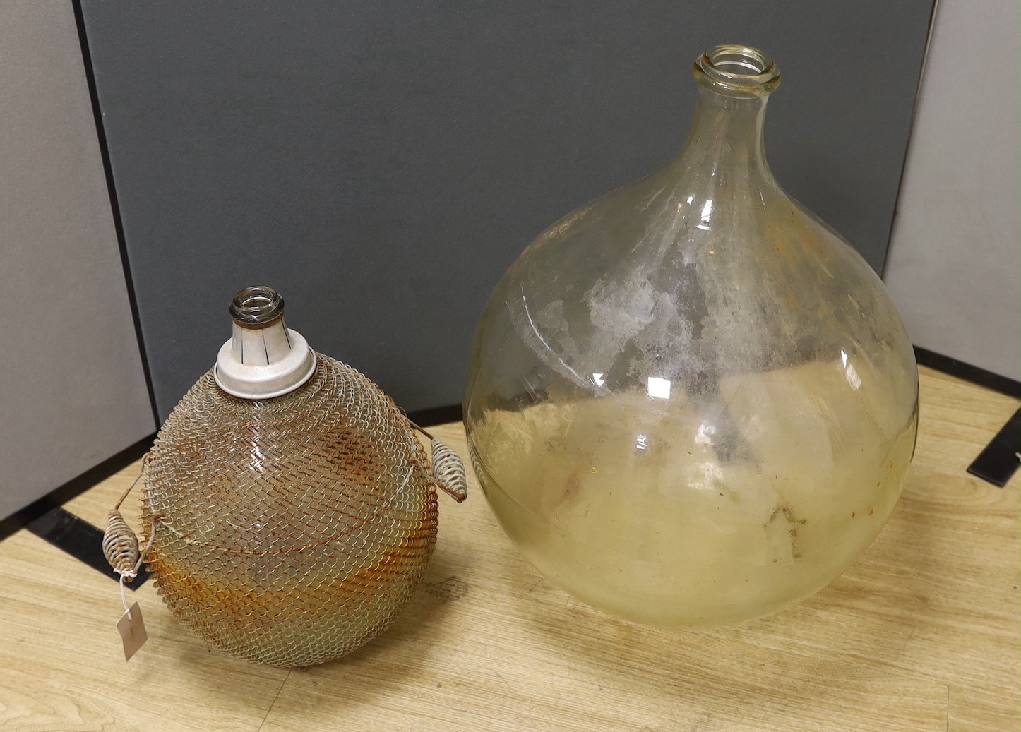 A large clear glass carboy and unusual wire-mounted glass carboy, largest 28cms high.